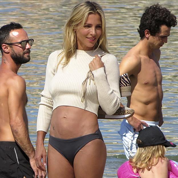 Elsa Pataky posando frente al mar con un cropped top blanco de manga larga y un bikini negro. 
