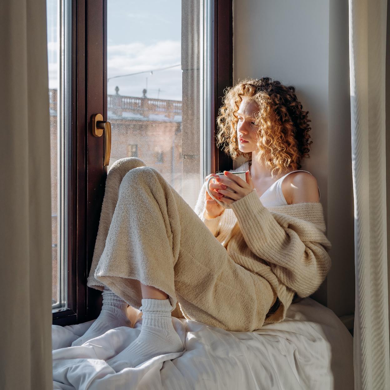 Mujer tomando una taza de infusión sentada frente a una ventana. 