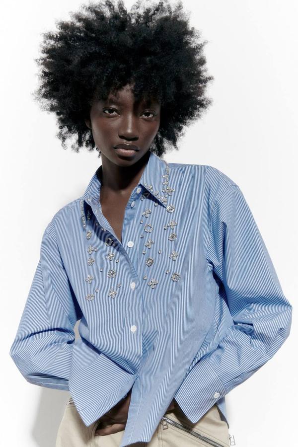 Camisa de popelín con cuello solapa, manga larga, cierre de botones, detalles de joyas y estampado de rayas en azul y blanco. Puedes encontrarla por 49,95 euros.