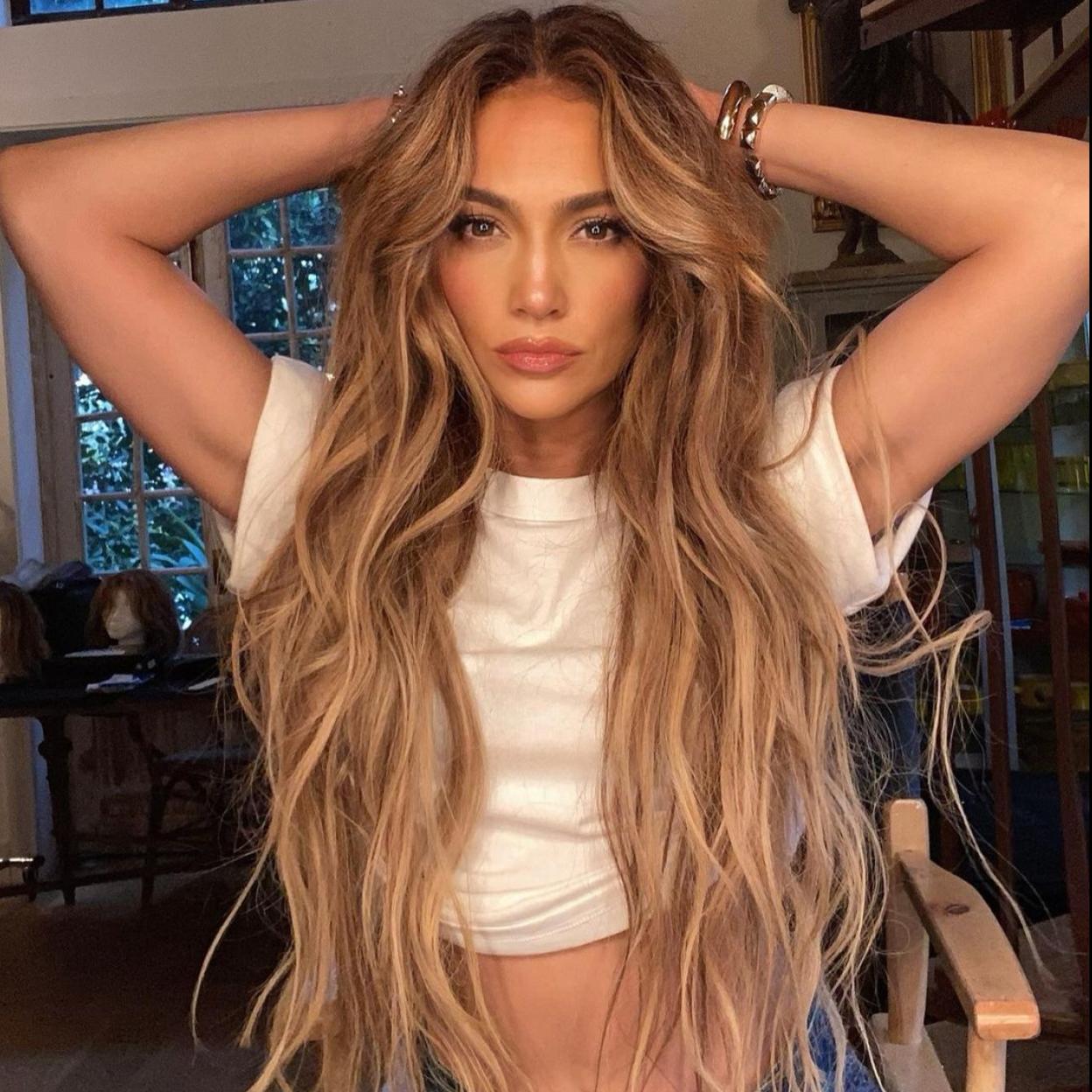 Jennifer Lopez con un cropped top blanco y unos pantalones vaqueros. 