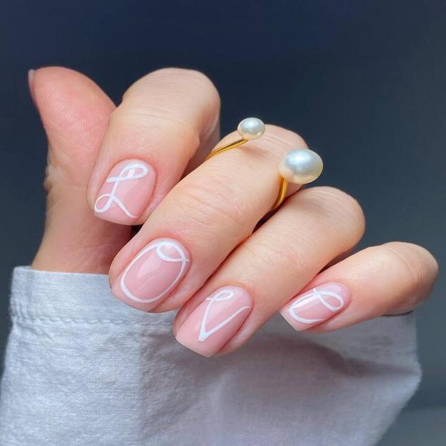 Si quieres que tus uñas envíen un mensaje, escoge una palabra de cuatro o cinco letras. Empieza por pintar las uñas con esmalte tono natural. El segundo paso es pintar las letras con una caligrafía bonita en esmalte blanco. Por ejemplo, puedes escoger la palabra love del diseño de la foto y en la uña que falta, dibuja un corazón o píntala entera de blanco, otro color o con glitter.