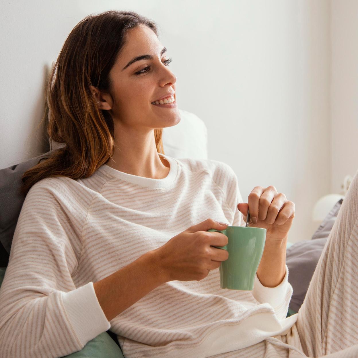 Mujer tomando una infusión en la cama. 