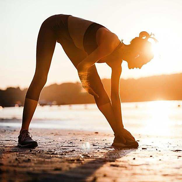 Mujer estirando después de hacer ejercicio al atardecer. 