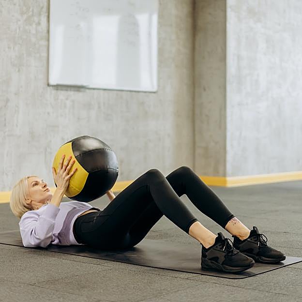 Mujer realizando crunch abdominal sobre una fitball. 
