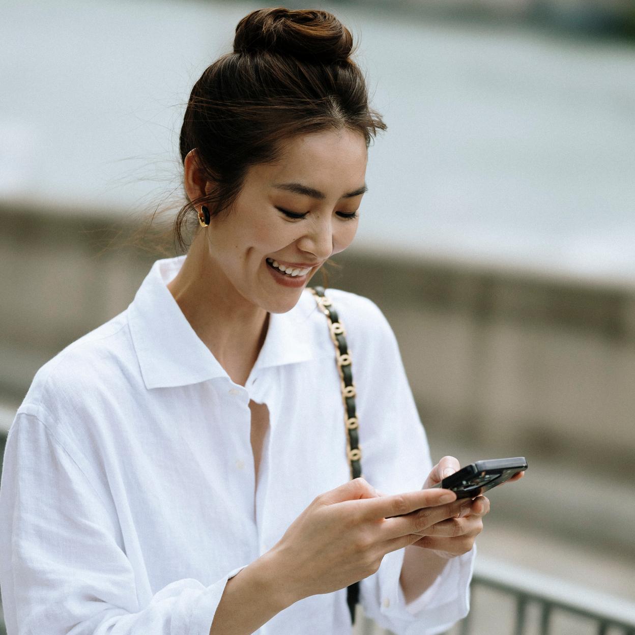 Una mujer con camisa blanca consultando el móvil.