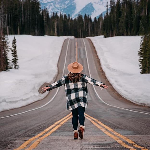 Mujer con camisa de cuadros andando por una carretera en un entorno nevado 