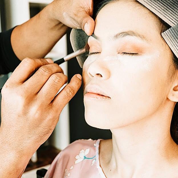 Maquillador aplicando sombra de ojos a mujer