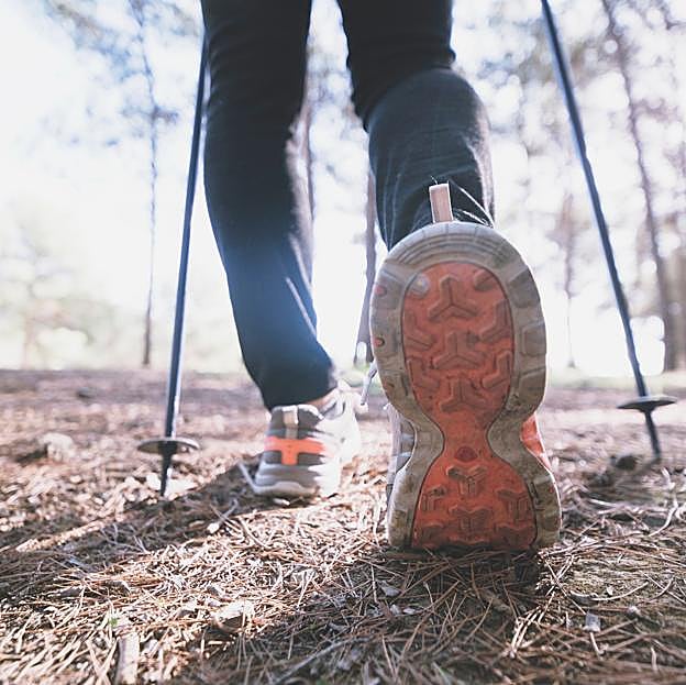 Mujer caminando por el bosque con la ayuda de unos bastones. 