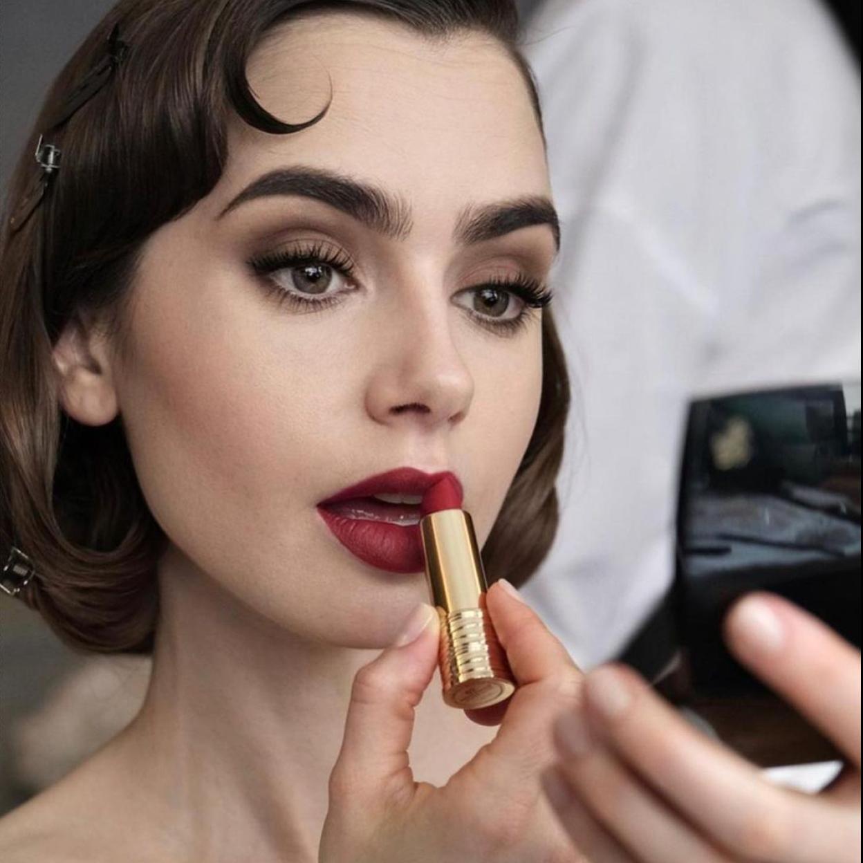 La actriz Lily Collins pintándose los labios de rojo.