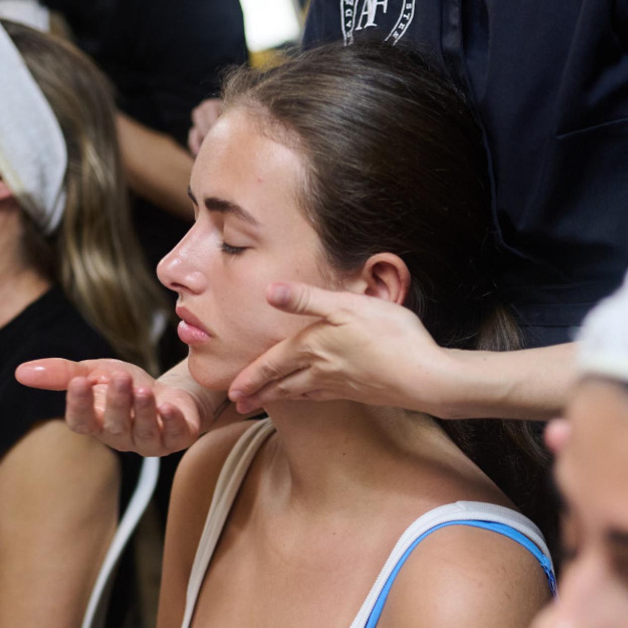 Unas modelos en el backtage recibiendo masajes faciales.