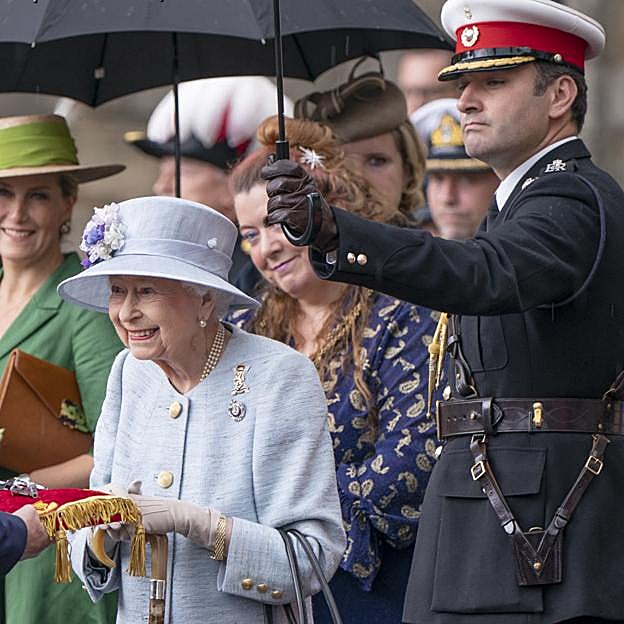 El coronel Tom White protegiendo de la lluvia a Isabel II.