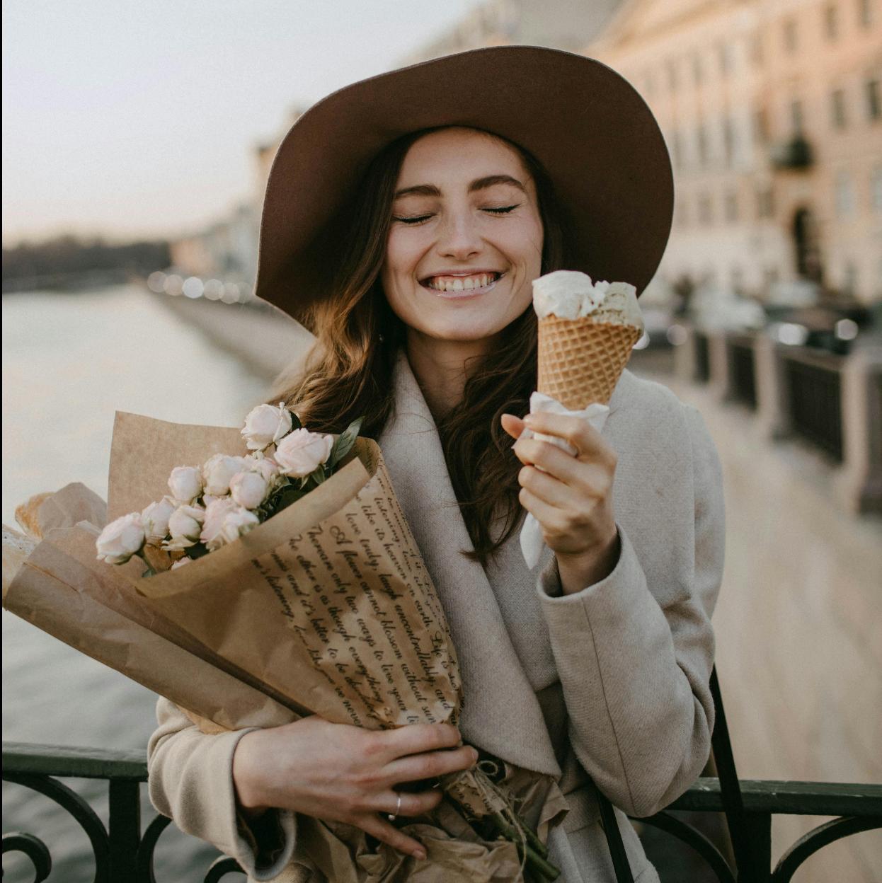 Mujer feliz tomando helado y sosteniendo flores. 