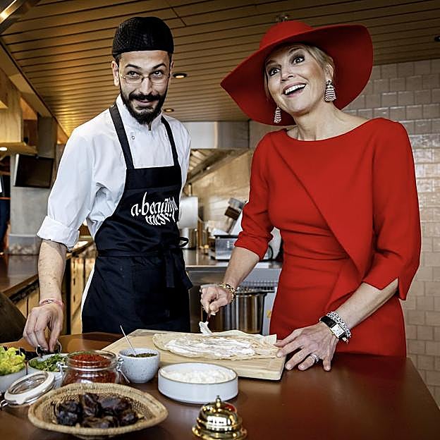 La reina Máxima, de rojo y con sombrero en un restaurante.