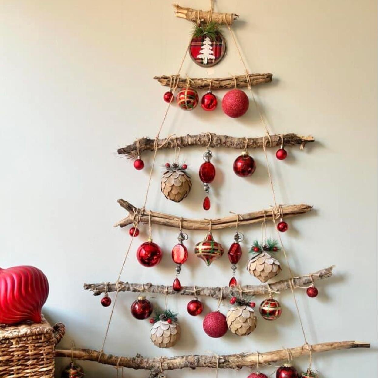 Árbol de Navidad de pared hecho con palos, cuerdas y adornos en color rojo.