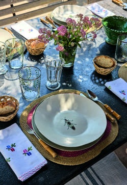 Imagen secundaria 2 - Arriba, rincón de la cocina, con azulejos antiguos recuperados de Antic Alaior, lámpara en suspensión portuguesa, de Candelabro, y antigua pìla de piedra. A la derecha, detalle de la mesa con vajilla de insectos de Sena Cifuentes y vasos de vidrio pintados a mano de Agua Clara. A la izquierda, el perchero de la entrada con toda la impresionante colección de sombreros y cestas de madre e hija.
