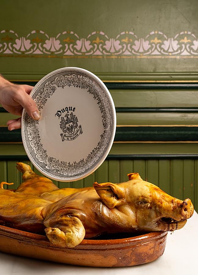 Imagen - El cochinillo asado, a punto de ser cortado al estilo tradicional, con un plato. / DR