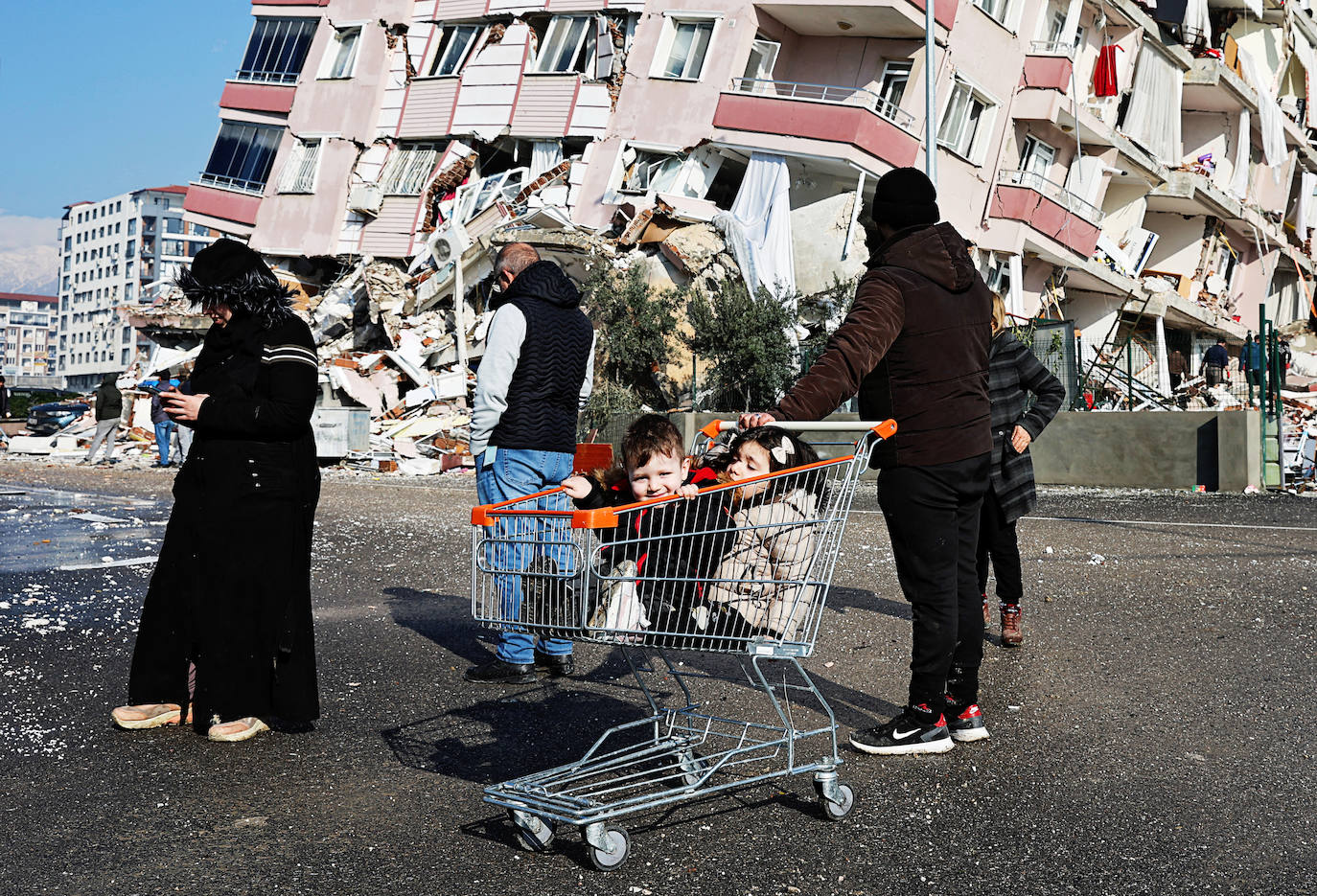 Niños sentados en un carrito de la compra cerca de un edificio derrumbado tras un terremoto en Hatay, Turquía. / UMIT BEKTAS (REUTERS)