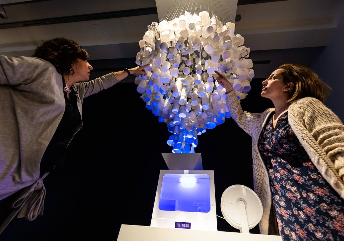 Dos mujeres tocan una trituradora para reciclaje en la exposición 'PRINT3D. Reimprimir la realidad' de CaixaForum Madrid.