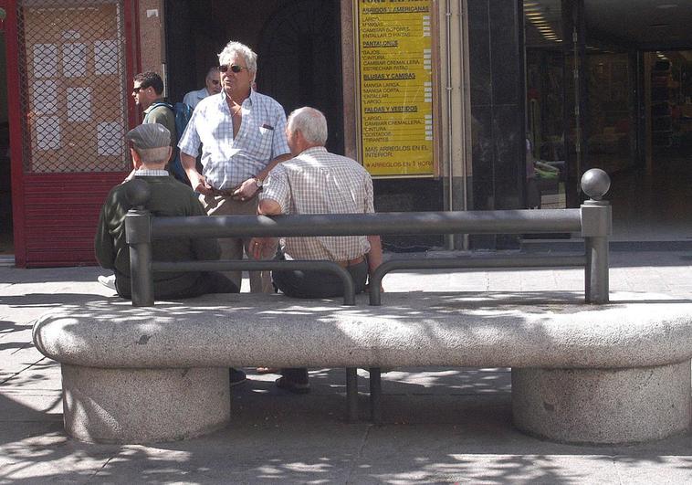 Un grupo de jubilados conversa en un banco.