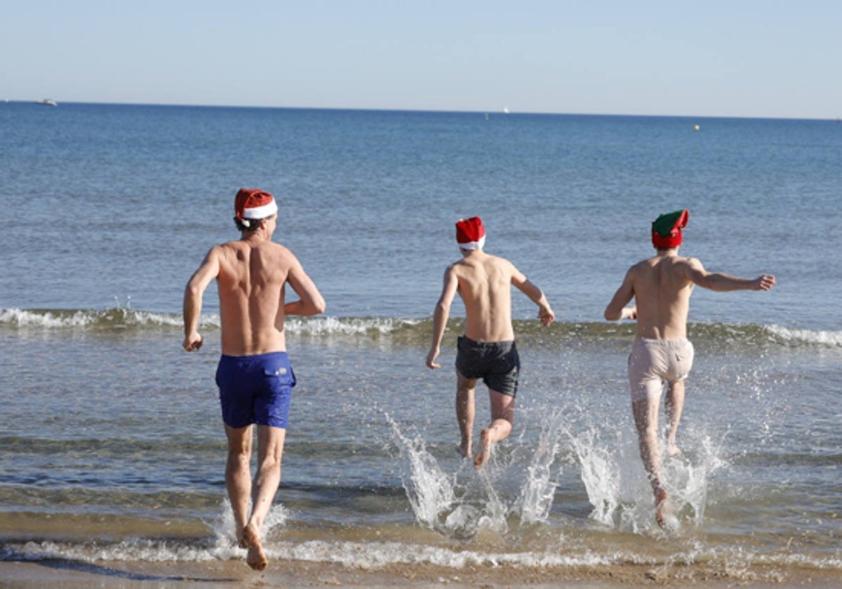 Tres jóvenes con gorritos de Papa Noel se zambullen en la orilla de una playa valenciana las pasadas Navidades.