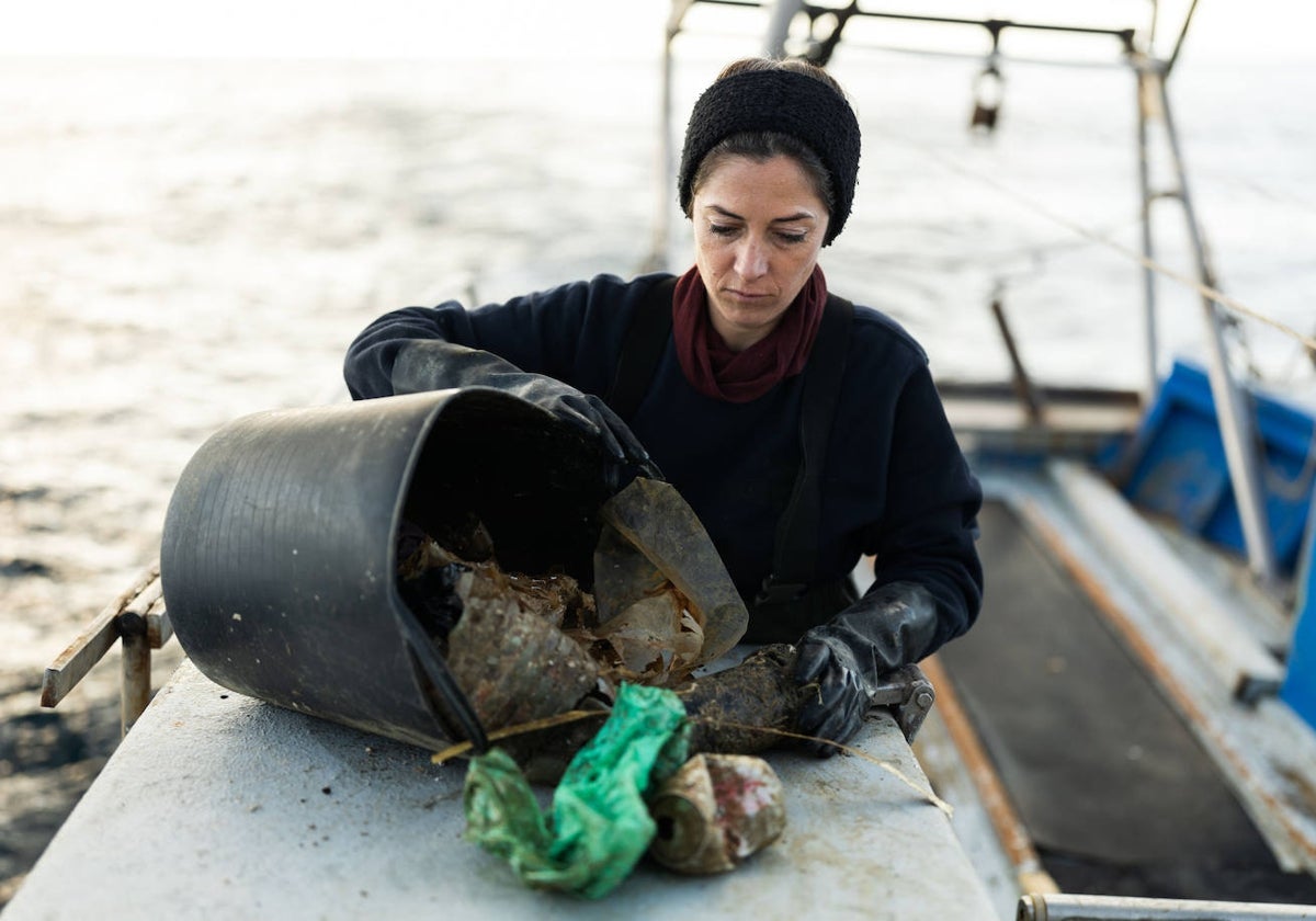 Miriam Artacho, en su barco de pesca, saca botellas de plásticos y latas recogidas en su red.