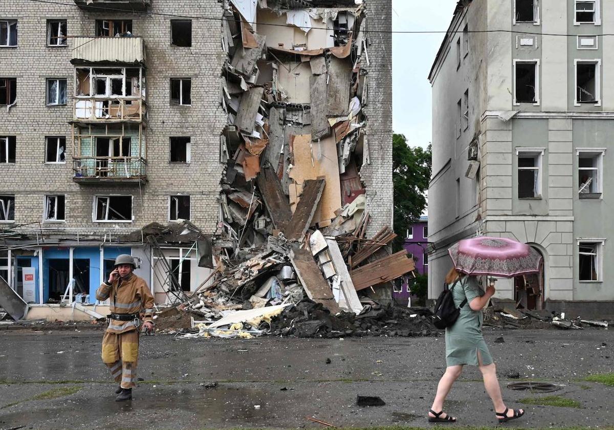 Una mujer pasa junto a un rescatista ucraniano que trabaja frente a un edificio parcialmente destruido tras un ataque con misiles rusos en Járkov.