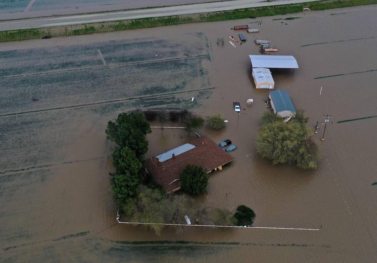 Una imagen aérea muestra una casa, vehículos y tierras de cultivo inundados durante una tormenta en el condado de Tulare, en California.