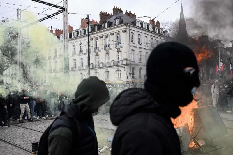Dos radicales caminan frente a un escenario de destrucción durante una manifestación en Nantes.