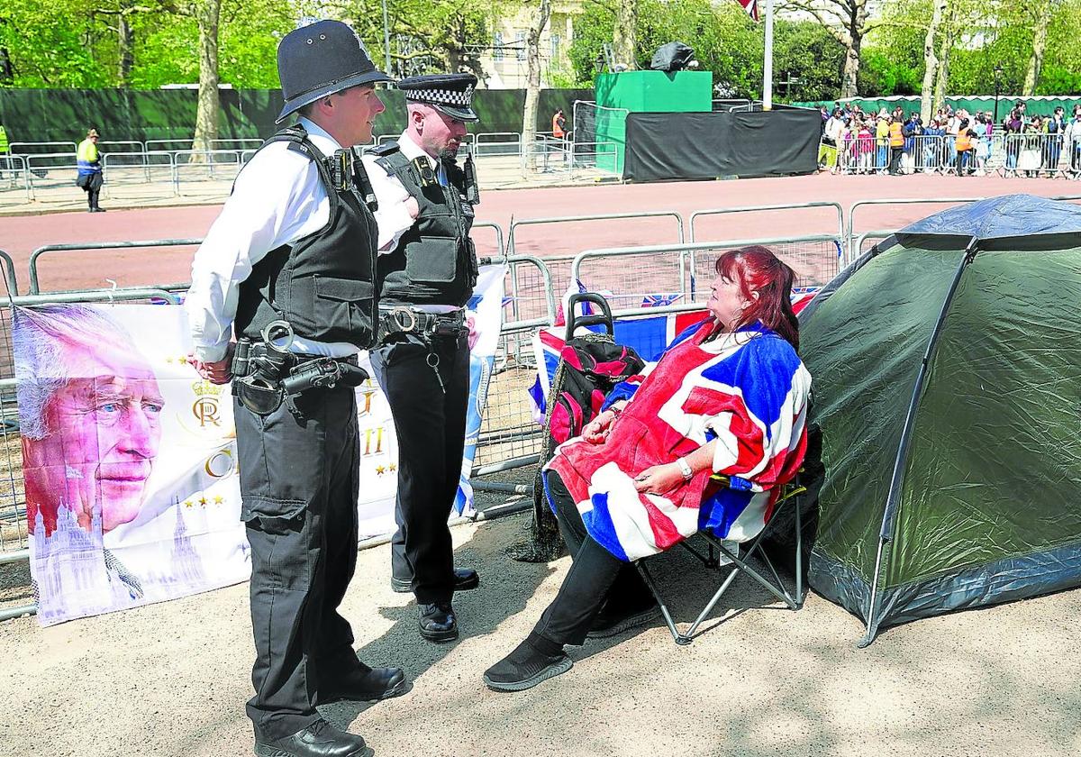 Dos agentes charlan con una mujer enfundada en la Union Jack que ha conseguido un lugar privilegiado para ver mañana a Carlos III.