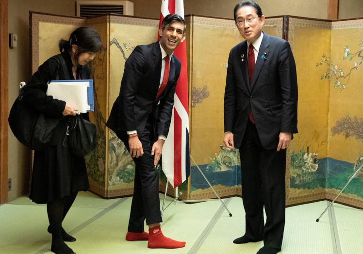 Insólita imagen en la que el primer ministro británico, Rishi Sunak, muestra sus calcetines con el logo del club de béisbol Hiroshima Toyo Carp. a su homólogo japonés, Fumio Kishida, seguidor de este equipo.