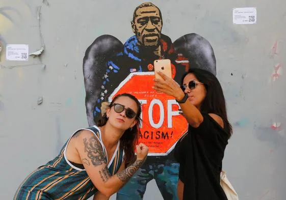 Dos mujeres se retratan junto una imagen George Floyd, muerto por la brutalidad policial en EE UU.