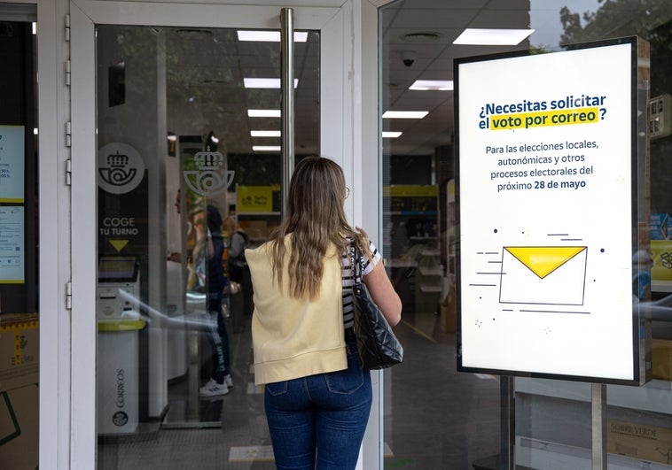 Una mujer entra a una oficina de Correos donde se anuncia el voto postal para estas elecciones