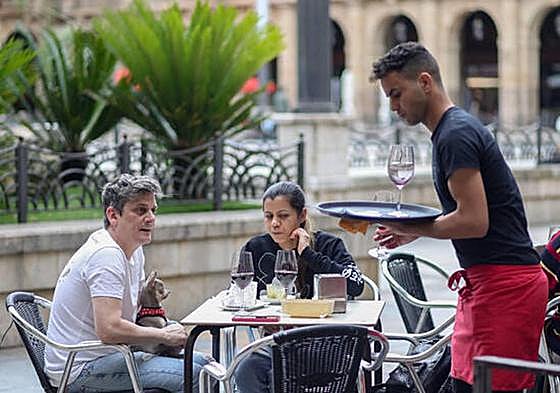 Unos clientes y un camarero en la terraza de un bar.
