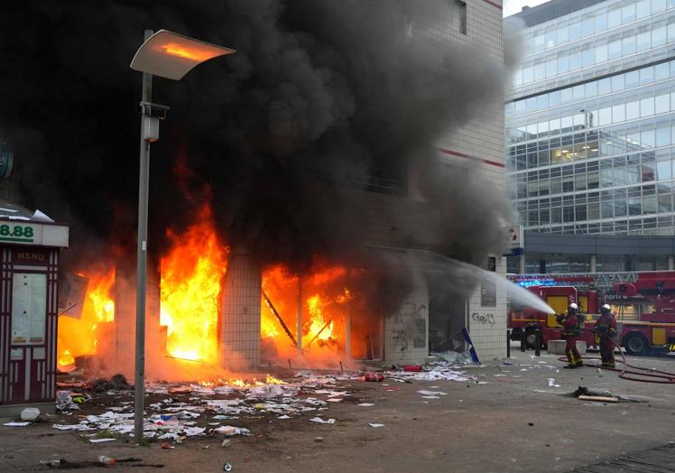 Los bomberos intentan apagar el incendio provocado en una entidad financiera en un barrio de París.