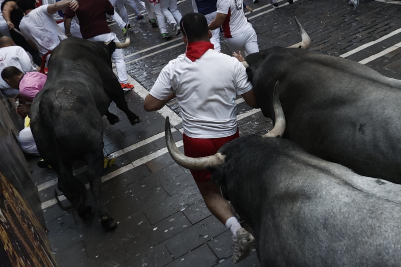 Un mozo corre delante de los toros en la calle Estafeta tras pasar la curva de Mercaderes.