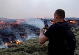 Un hombre toma una fotografía de la erupción de un volcán cerca de Reykjanes, capital de Islandia