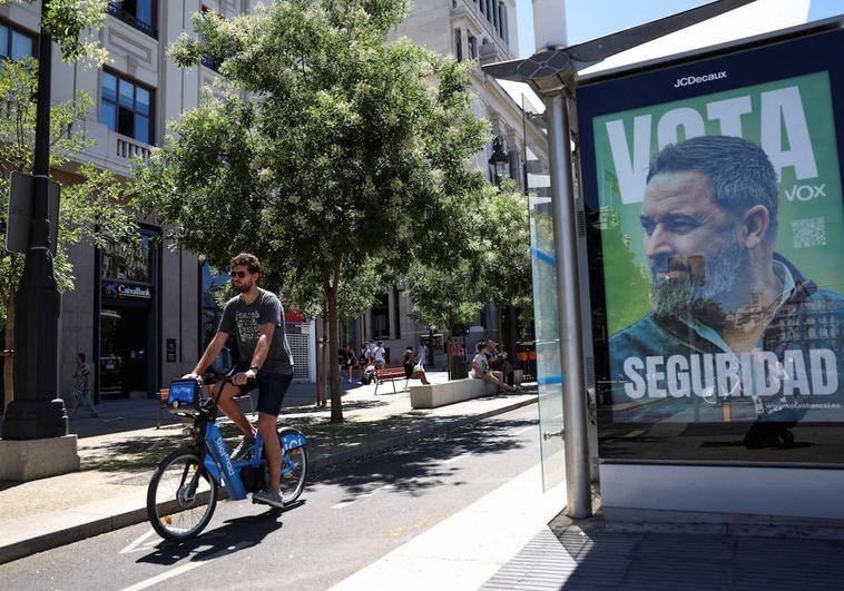 Un joven pasea en bicicleta junto a un cartel electoral de Vox.
