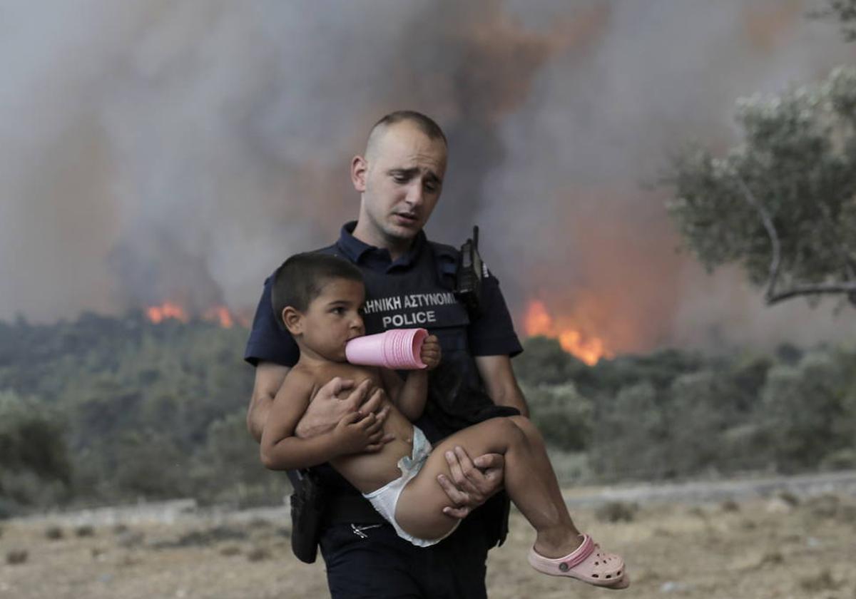 Un policía griego ayuda a evacuar a un niño de un incendio forestal cerca de Atenas