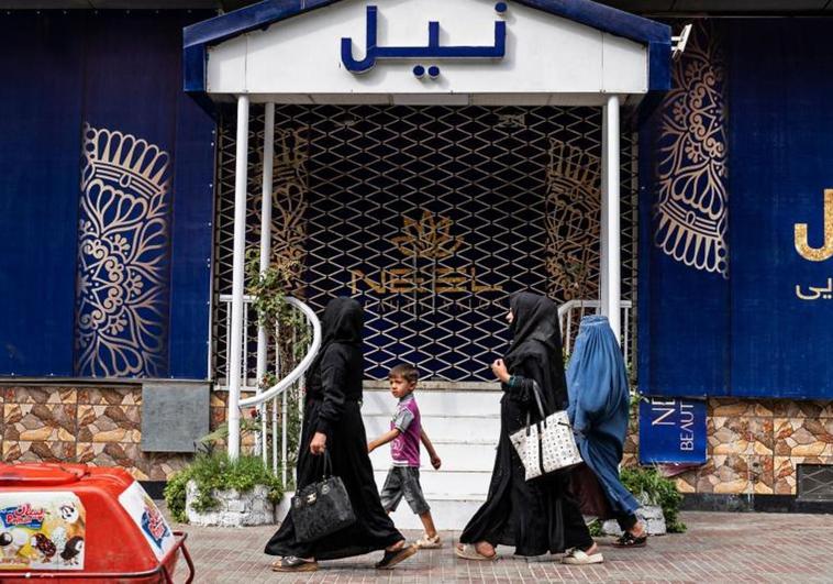 Mujeres afganas pasan frente a un salón de belleza cerrado en Kabul.