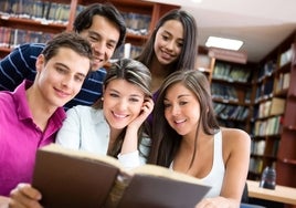 Un grupo de universitarios consulta un libro en la biblioteca.