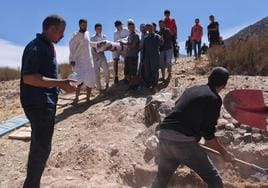Varias personas preparan la tumba de un hombre fallecido que ha sido encontrado entre los escombros