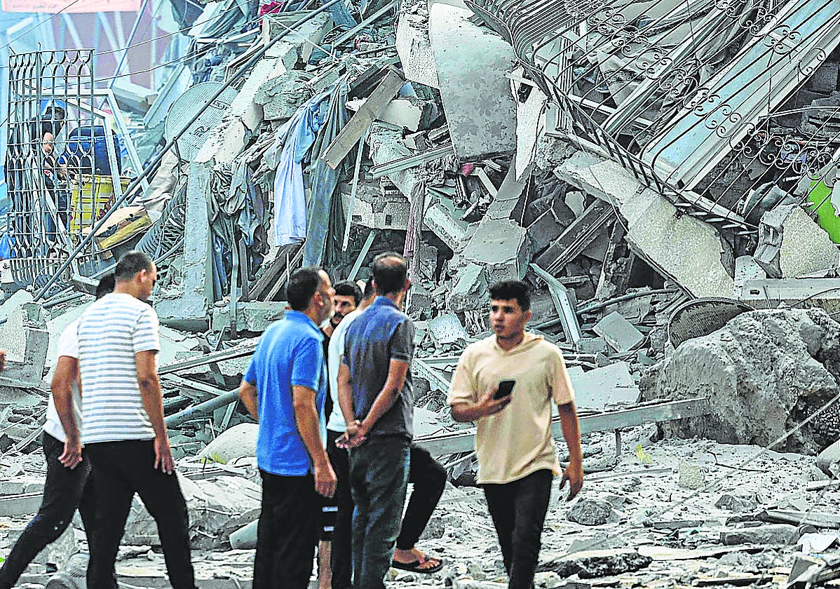 Un grupo de gazatíes observa los escombros de un edificio destruido por la aviación israelí.