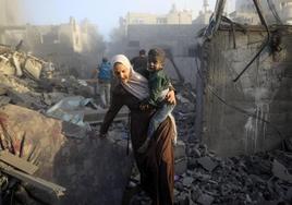 Una mujer con un niño en sus brazos huye de los ataques aéreos israelíes contra un campo de refugiados en la Franja.