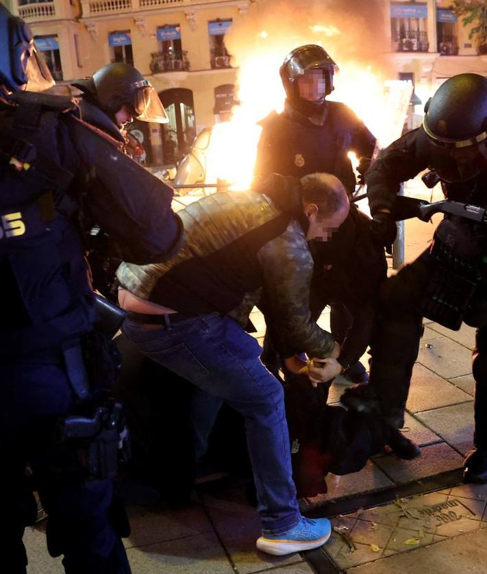 Imagen secundaria 2 - En la imagen superior, los agentes tratan de alejar a los manifestantes tras un primer conato de carga; en la foto siguiente, un antidisturbios persigue a un joven que estaba en la zona de los alborotadores y, por último, varios policías detienen a uno de los sospechosos de los altercados violentos mientras detras suyo arde un contenedor incendiado por los ultras en la calle Ferraz.