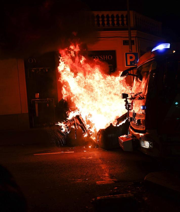 Imagen secundaria 2 - En la imagen superior, radicales y encapuchados se hicieron una noche más con la cabecera de la concentración de protesta a última hora; debajo, dos policias antidisturbios agarran a una persona envuelta con la bandera española y, por último, uno de los contenedores que fueron quemados por los violentos cerca de la madrileña calle Ferraz durante los altercados.