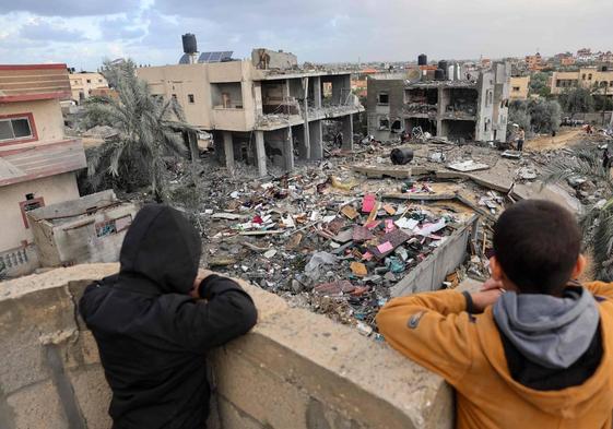 Niños palestinos observan a la gente parada entre los escombros de un edificio destruido durante los ataques israelíes en Rafah.