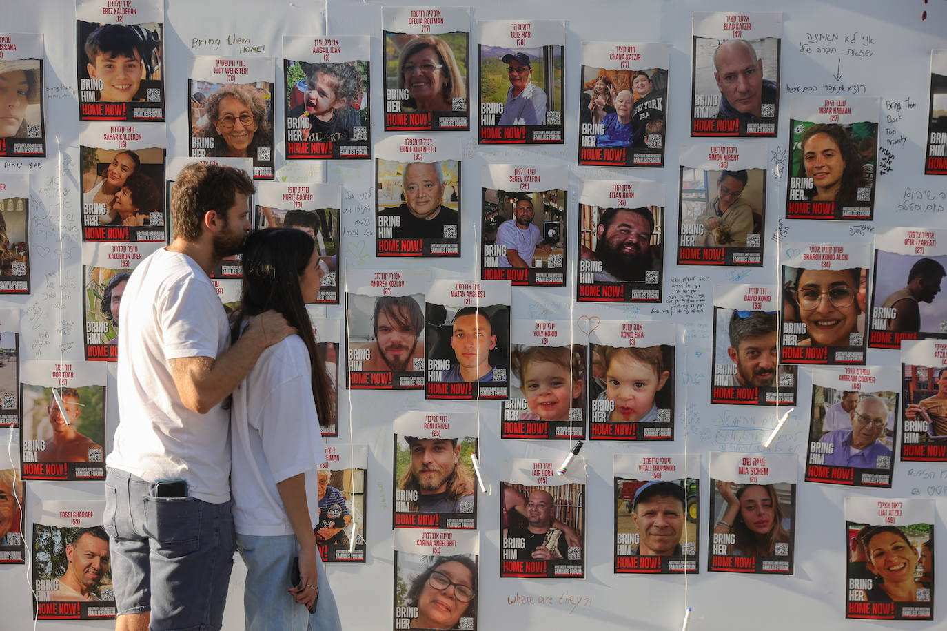 Una pareja pasa junto a las fotos de los rehenes en Tel Aviv.