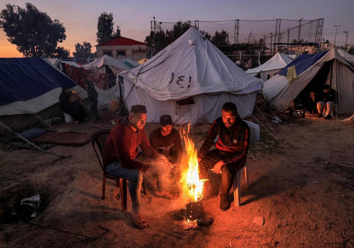 Los palestinos se calientan alrededor de un fuego fuera de una de las tiendas que albergan a los desplazados por el conflicto en Gaza.