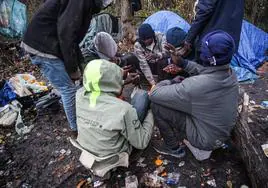 Migrantes sudaneses se sientan junto al fuego cerca de sus tiendas de campaña en Calais, en Francia