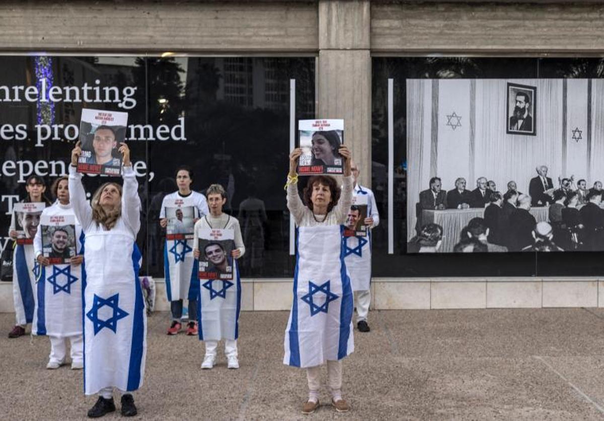 Varias personas envueltas en banderas israelíes sostienen retratos de algunos de los rehene.